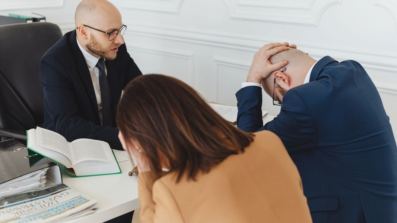 Legal professionals engaged in a tense meeting at a law office with open documents on the desk.