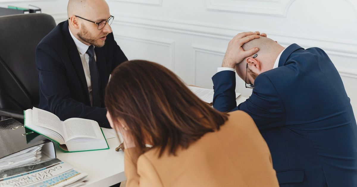 Legal professionals engaged in a tense meeting at a law office with open documents on the desk.