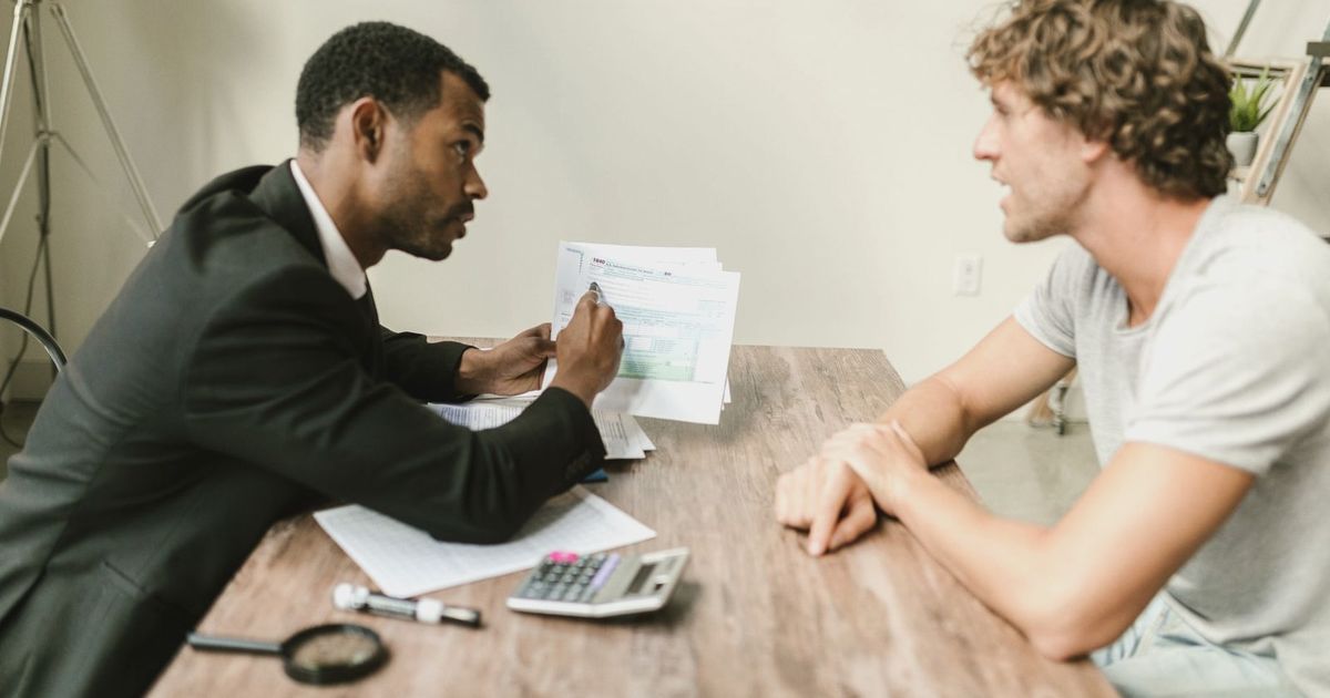 A financial advisor discusses paperwork with a client at a desk in a modern office.