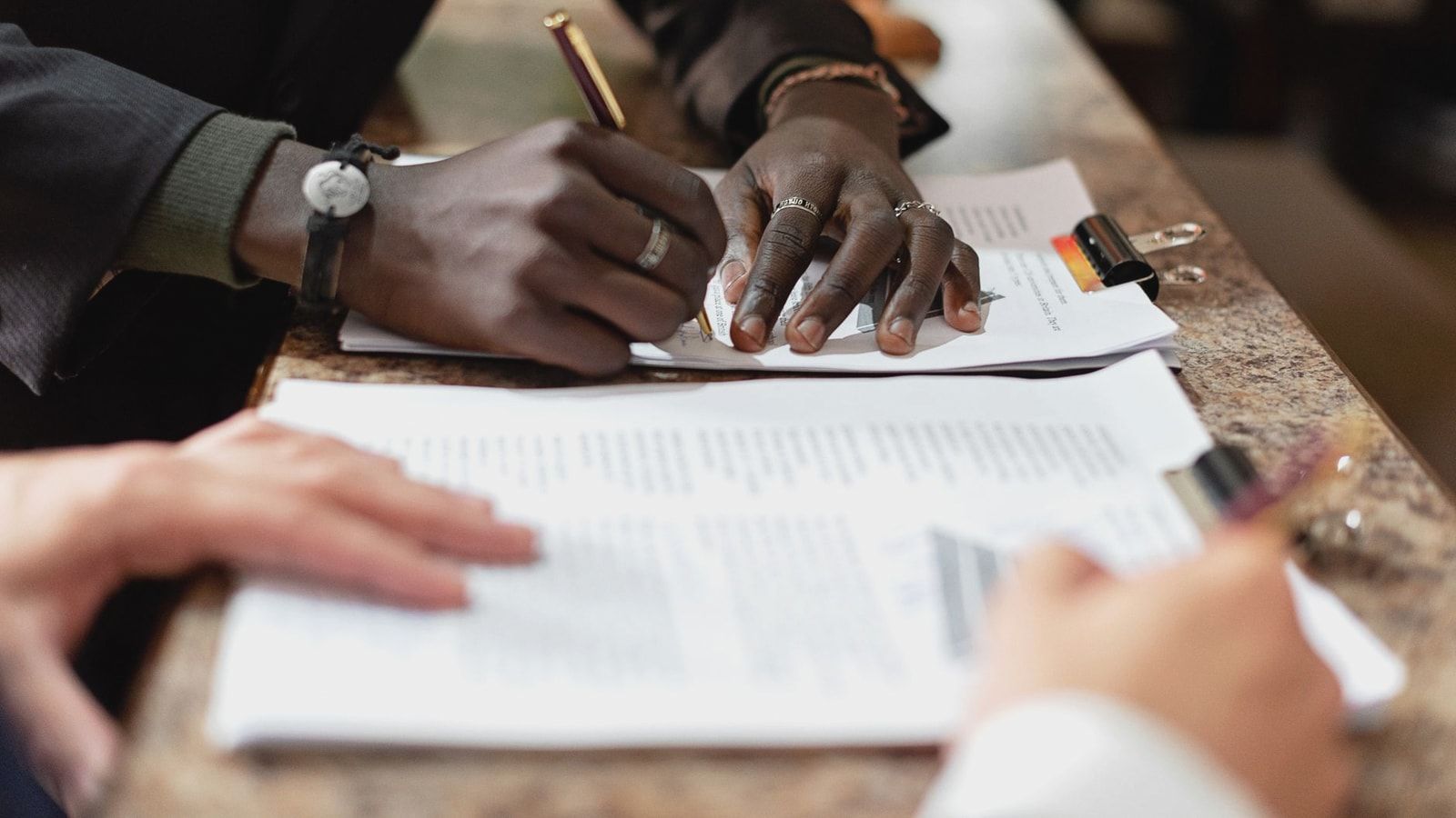 Close-up of hands signing documents in a business setting, emphasizing professionalism and teamwork.