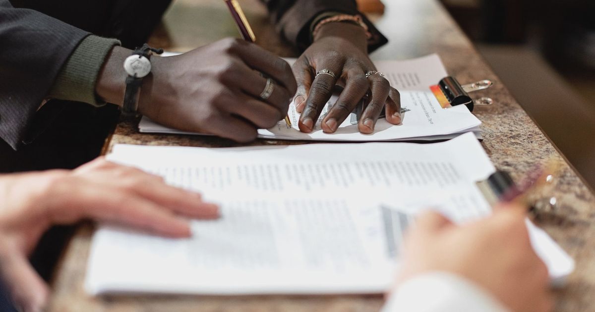 Close-up of hands signing documents in a business setting, emphasizing professionalism and teamwork.
