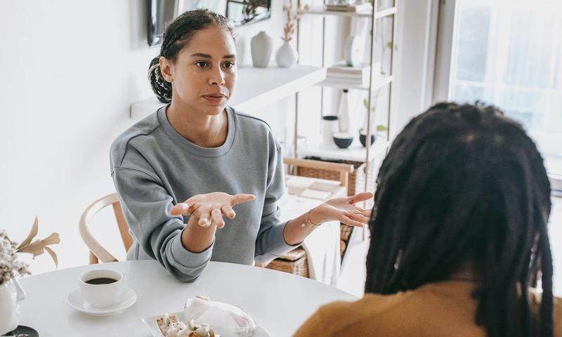 Young African American woman sitting at table and arguing with man in casual outfit in daylight