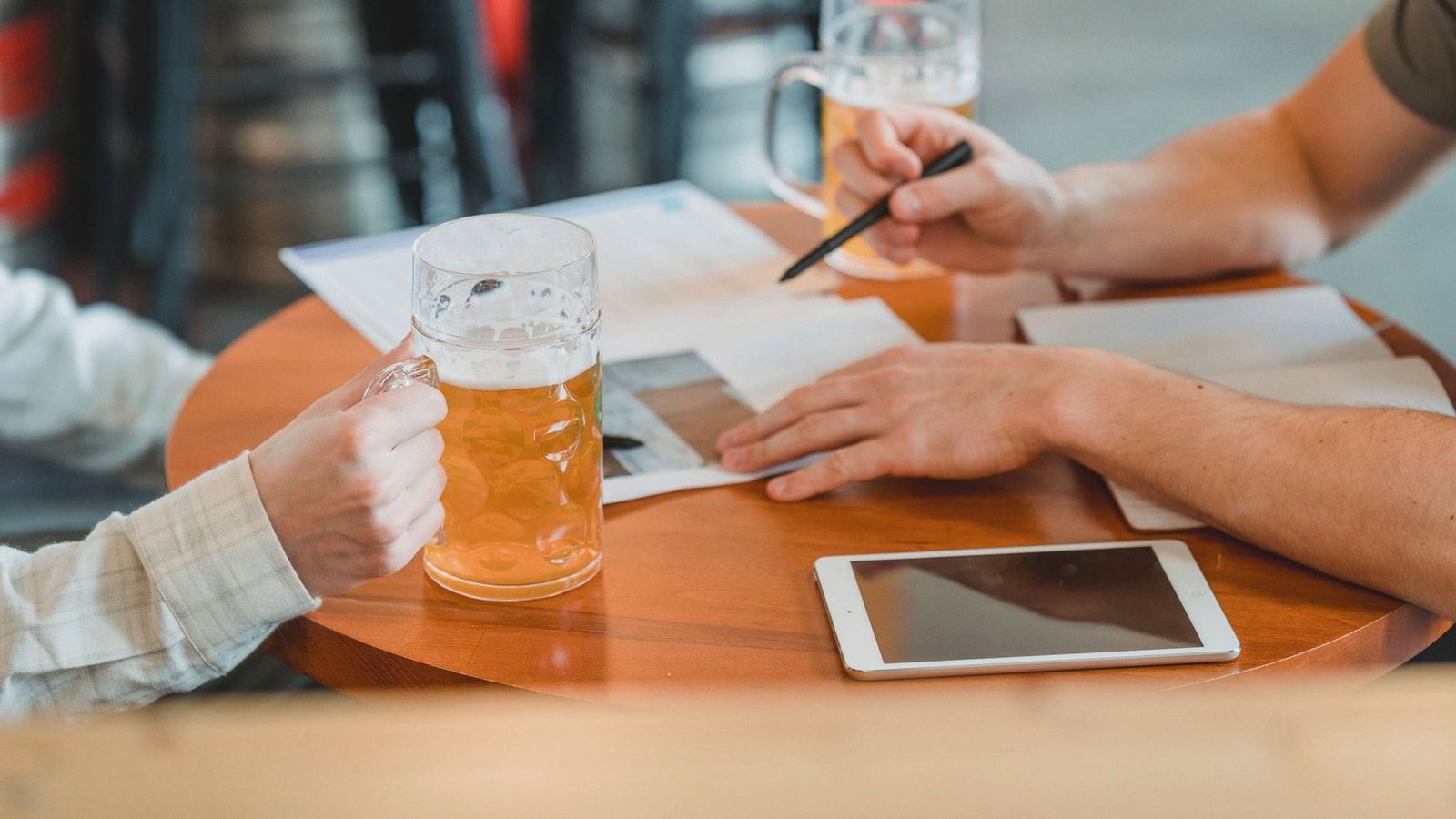 Side view of crop colleagues checking important papers near tablet and glasses of beer on table