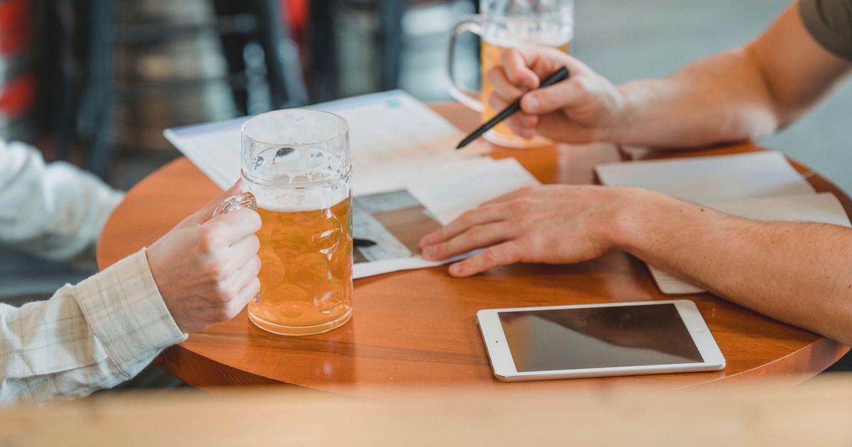 Side view of crop colleagues checking important papers near tablet and glasses of beer on table