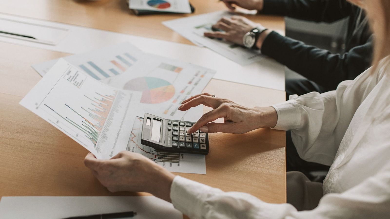 Hands performing financial calculations with charts and a calculator at a meeting table.
