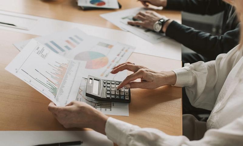 Hands performing financial calculations with charts and a calculator at a meeting table.