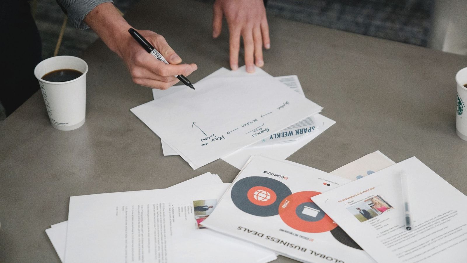 Two people collaborate during a business meeting, writing notes on papers with coffee cups nearby.