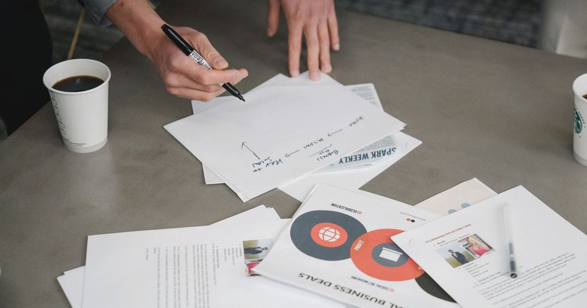 Two people collaborate during a business meeting, writing notes on papers with coffee cups nearby.