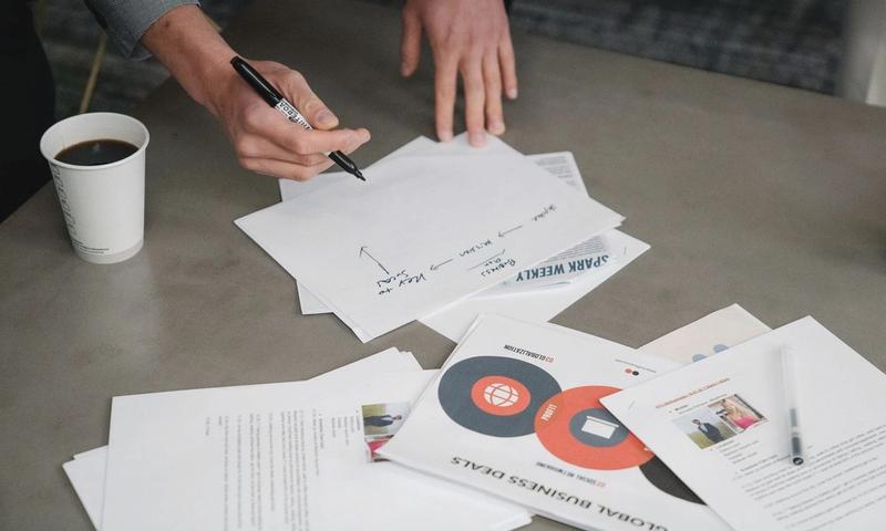 Two people collaborate during a business meeting, writing notes on papers with coffee cups nearby.