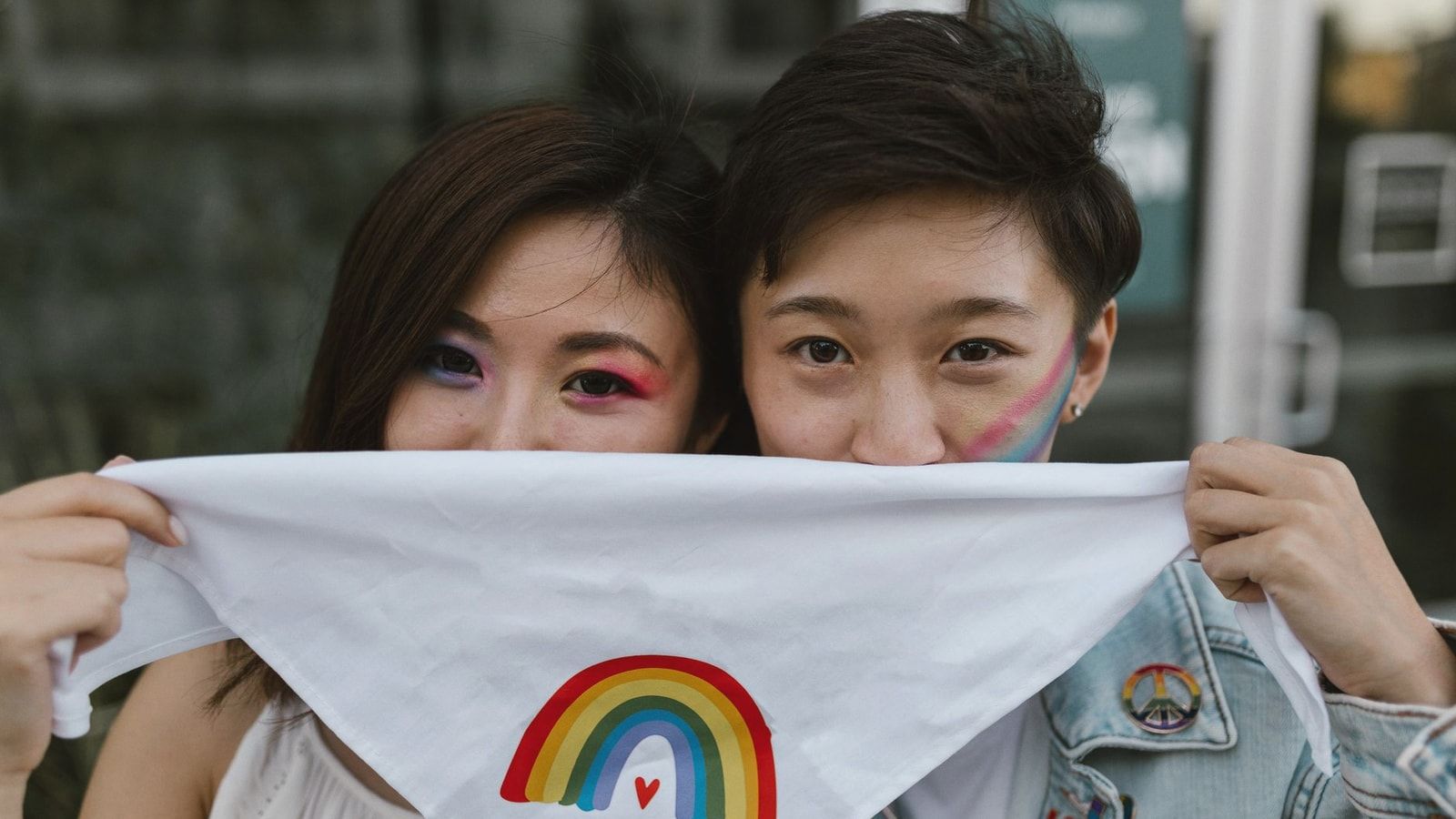 A couple with rainbow face paint holds a 'Love is Love' bandana, embracing love and diversity.