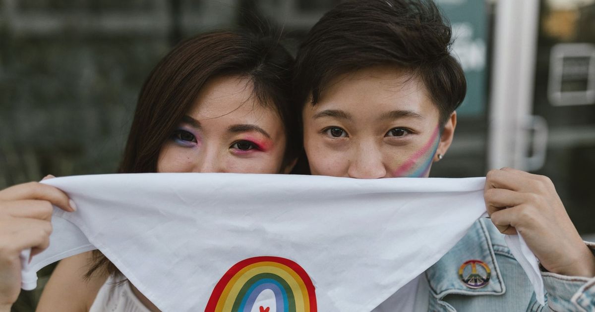 A couple with rainbow face paint holds a 'Love is Love' bandana, embracing love and diversity.