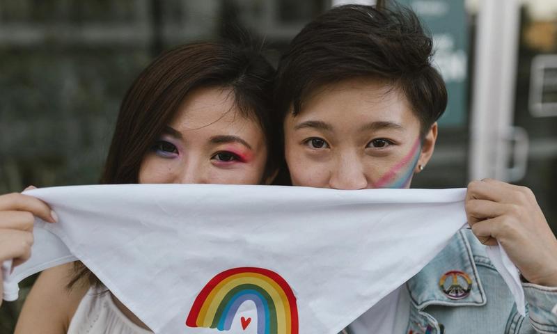 A couple with rainbow face paint holds a 'Love is Love' bandana, embracing love and diversity.