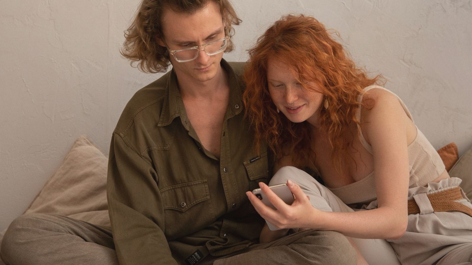 Calm couple in casual clothes browsing smartphone and looking at screen while resting together in light room in apartment
