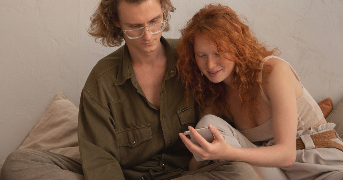 Calm couple in casual clothes browsing smartphone and looking at screen while resting together in light room in apartment