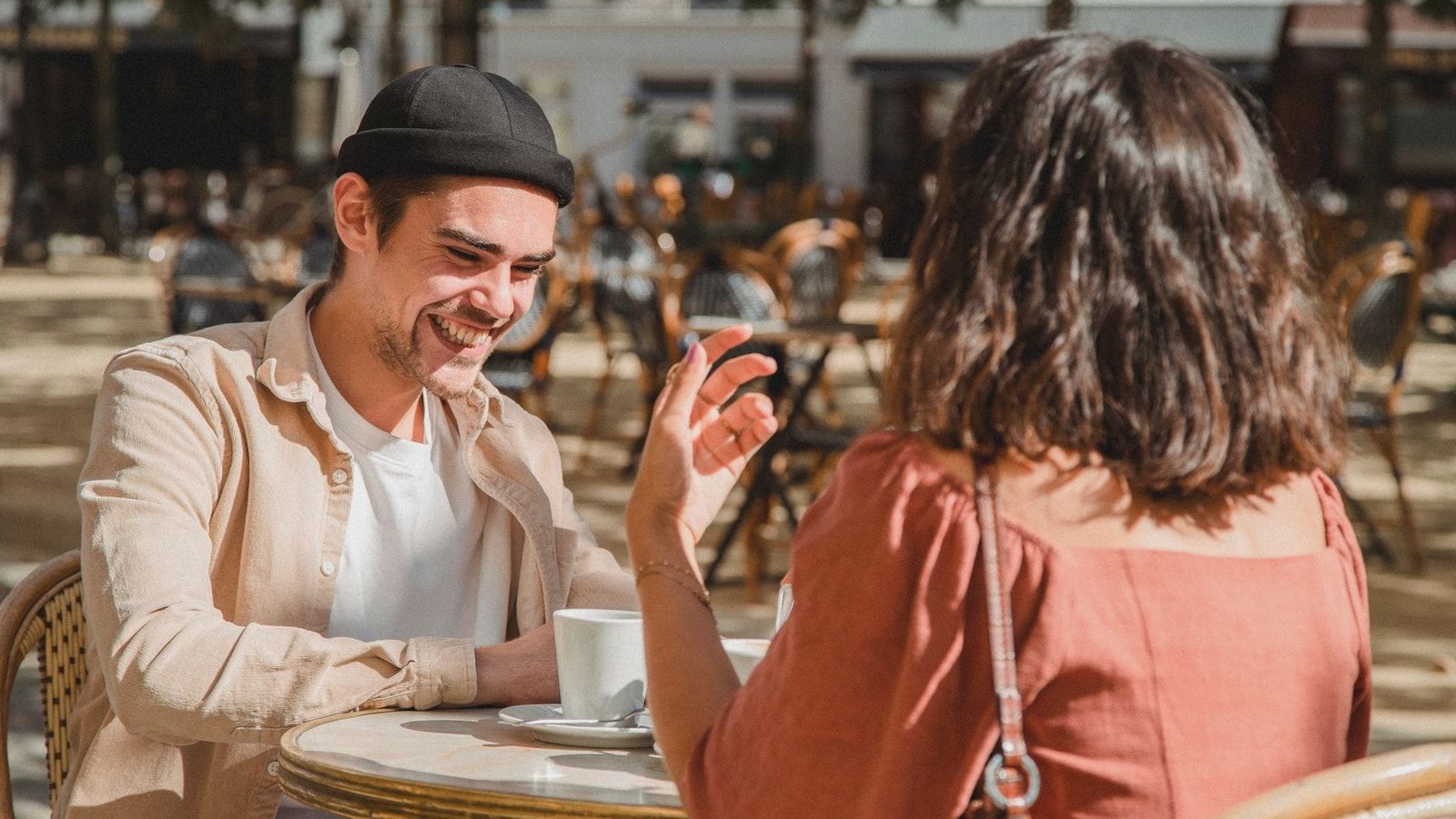Happy couple enjoying a sunny day at an outdoor cafe, sharing laughter over coffee.