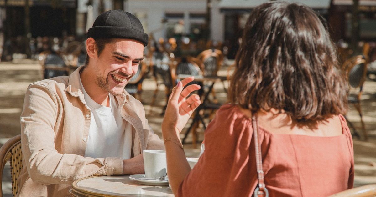 Happy couple enjoying a sunny day at an outdoor cafe, sharing laughter over coffee.
