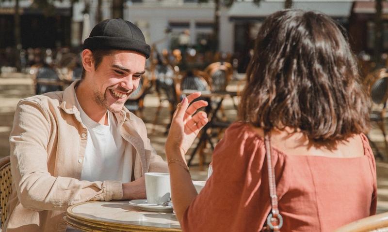 Happy couple enjoying a sunny day at an outdoor cafe, sharing laughter over coffee.