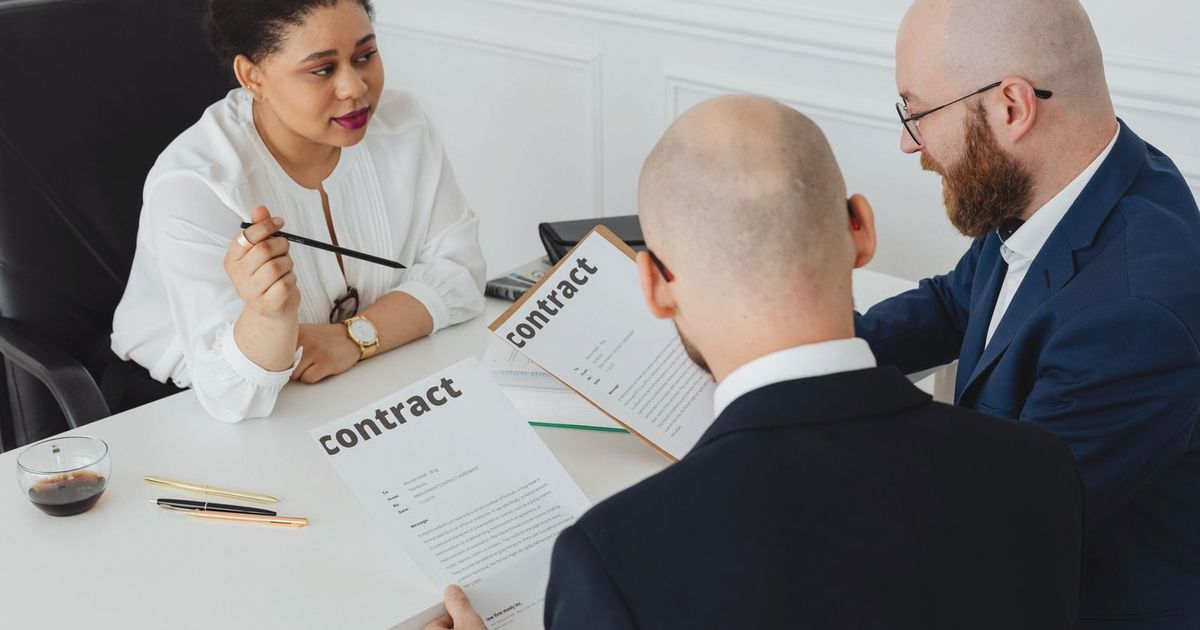Three business professionals in discussion over a contract in a modern office setting.