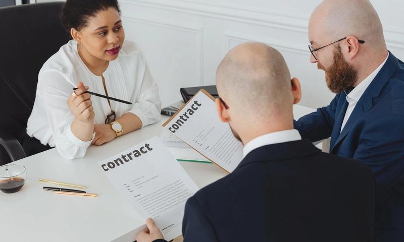 Three business professionals in discussion over a contract in a modern office setting.