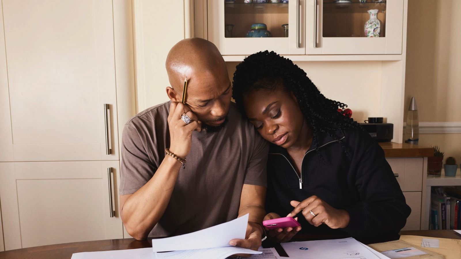 A couple sits at a table managing domestic finances, evaluating documents and using a smartphone.