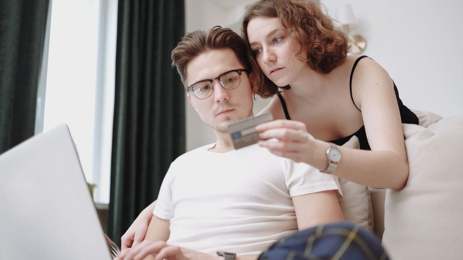 A young couple using a laptop and credit card for online shopping indoors.