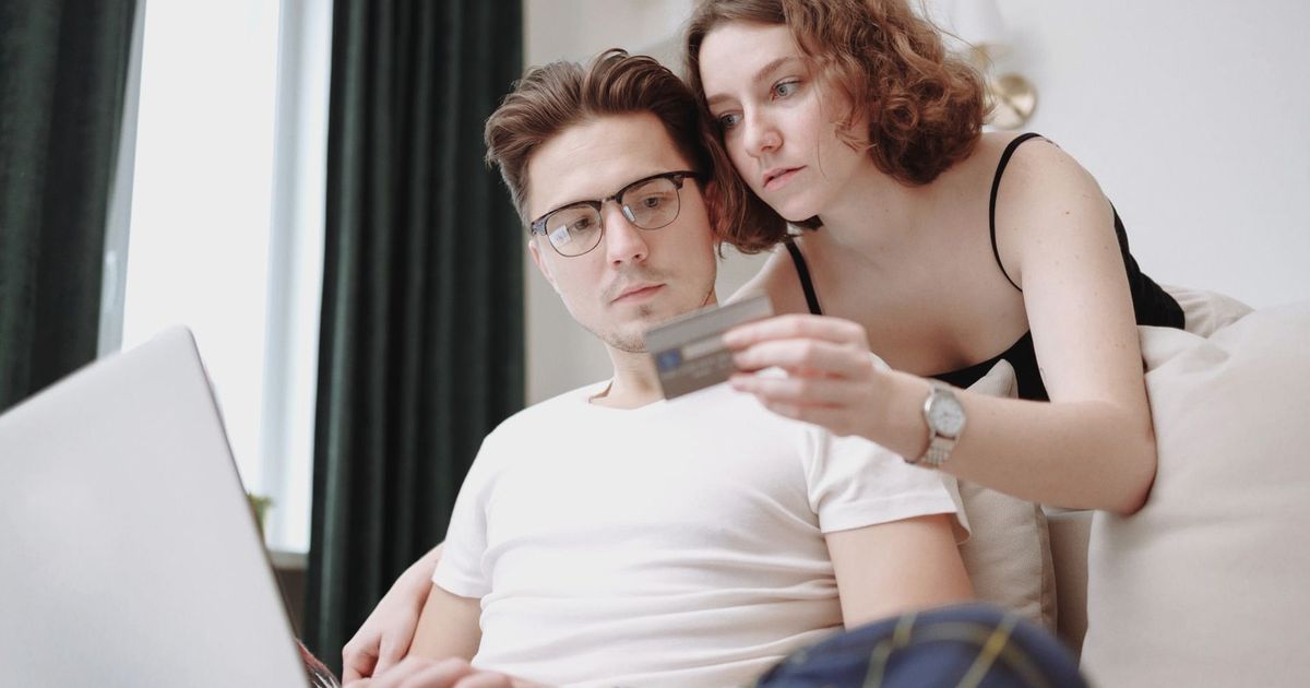 A young couple using a laptop and credit card for online shopping indoors.