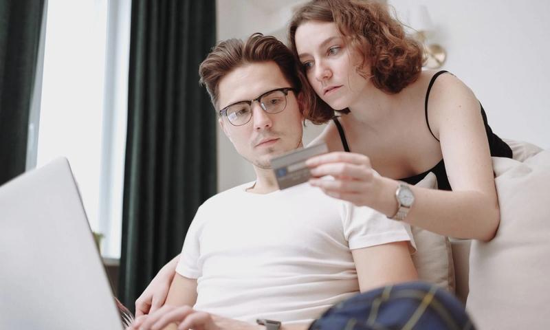 A young couple using a laptop and credit card for online shopping indoors.