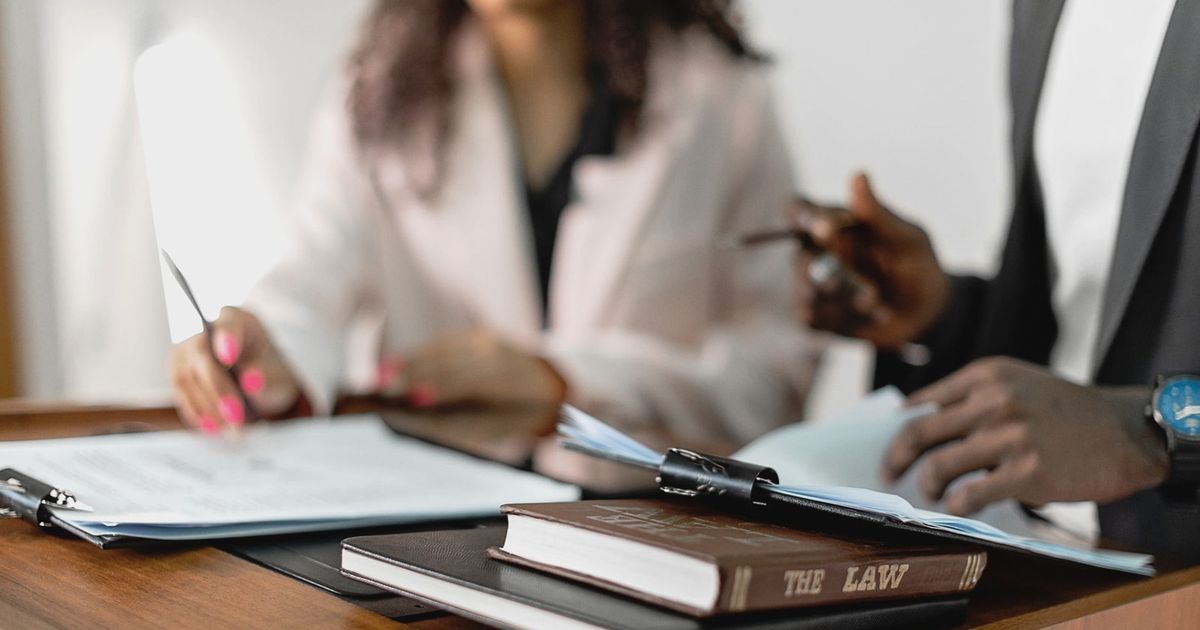 Two lawyers reviewing documents with law books on a desk. Professional legal environment.