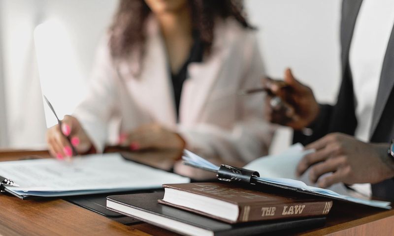 Two lawyers reviewing documents with law books on a desk. Professional legal environment.