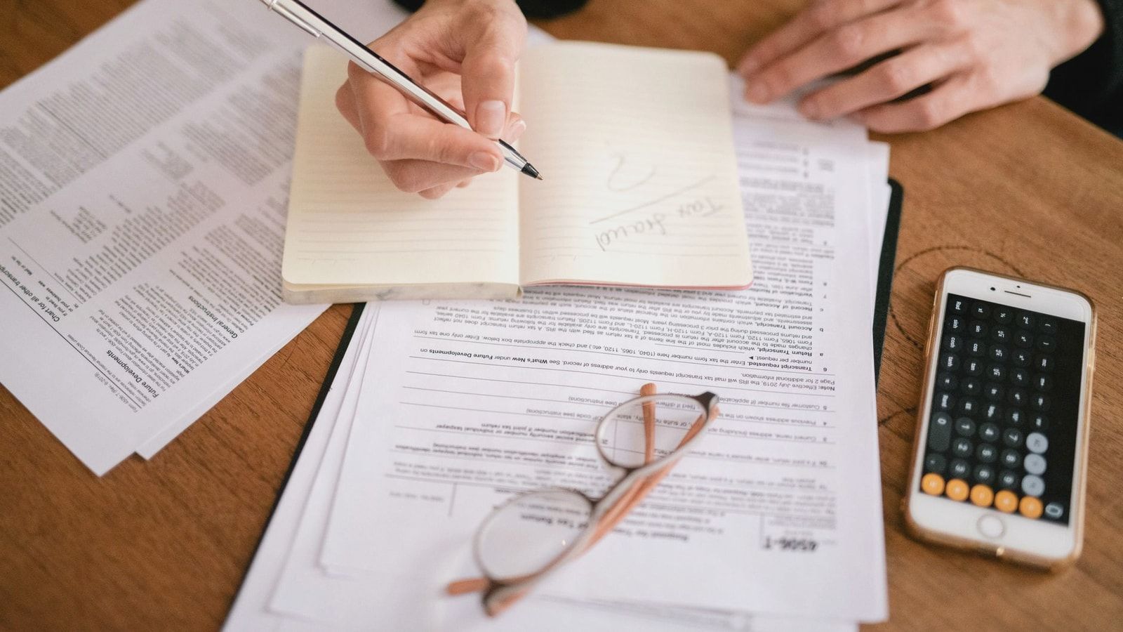 Close-up of a person writing in a notebook with documents and a calculator, managing finances.