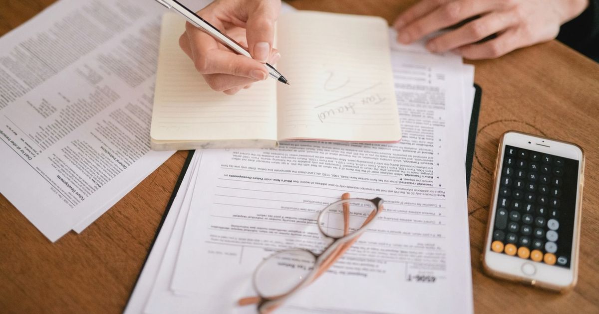 Close-up of a person writing in a notebook with documents and a calculator, managing finances.