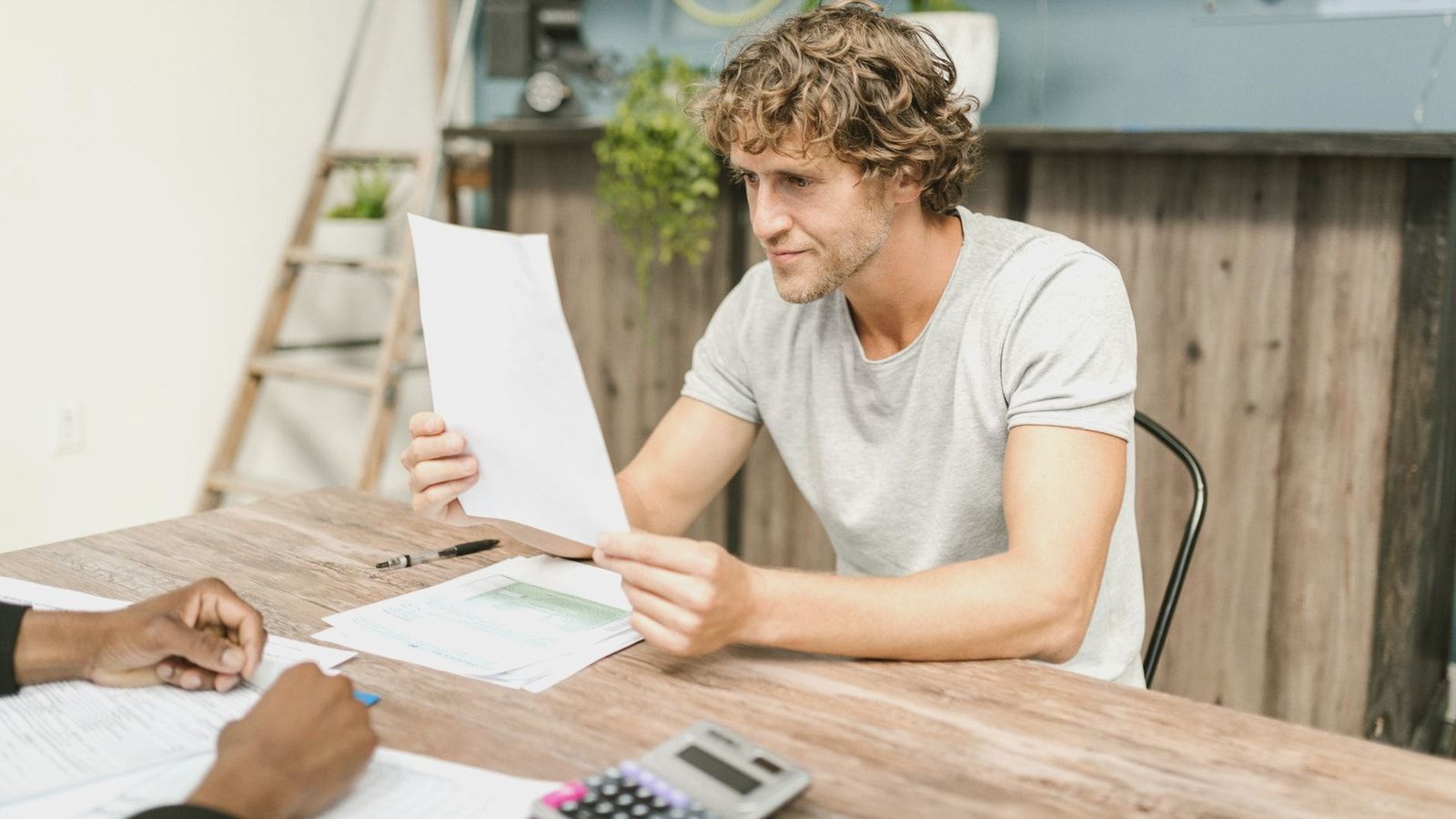 A man with curly hair evaluates documents at a desk, highlighting focused work in a professional setting.