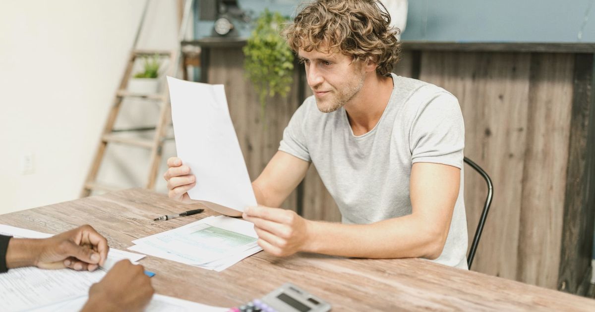 A man with curly hair evaluates documents at a desk, highlighting focused work in a professional setting.