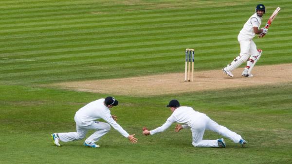 Two England fielders in Test whites dive for a low catch as the batter edges the ball during a Test match in Southampton
