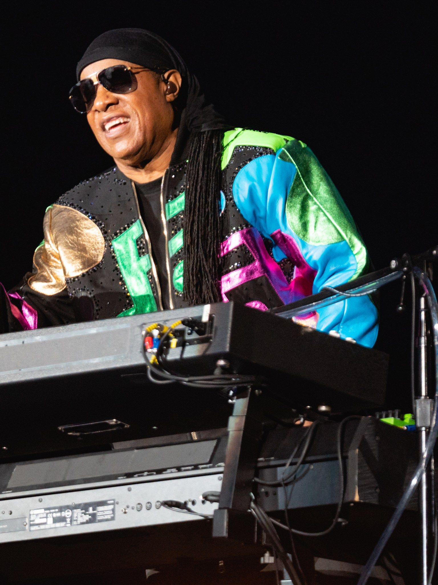 Stevie Wonder laughing as he plays keyboard on stage against a dark background