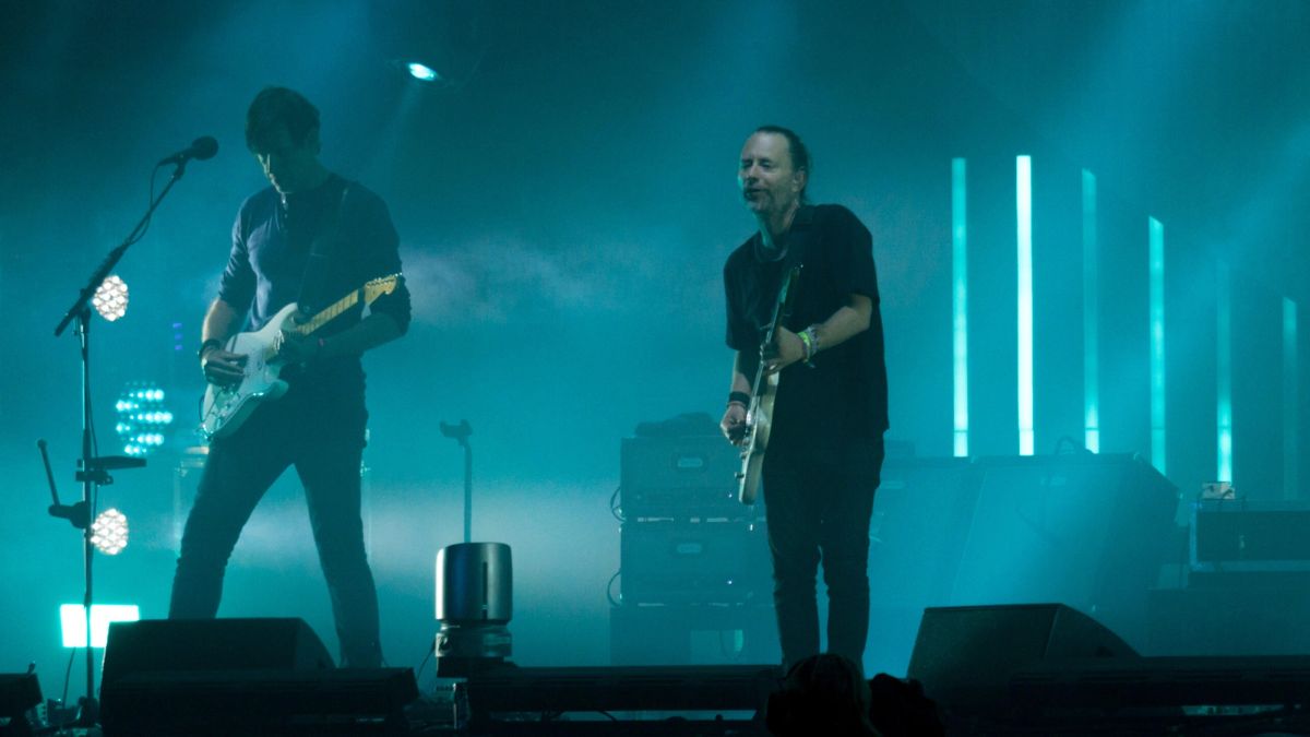 Thom Yorke & Jonny Greenwood perform Radiohead concert stage in blue-green light & fog.