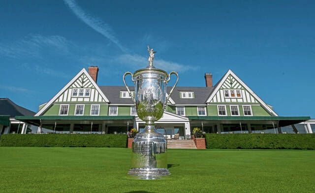 Gleaming U.S. Open Trophy on green lawn before prestigious clubhouse at major golf championship.