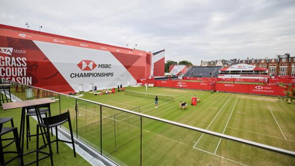 A hospitality terrace with high tables overlooking outer grass courts and HSBC branded boards