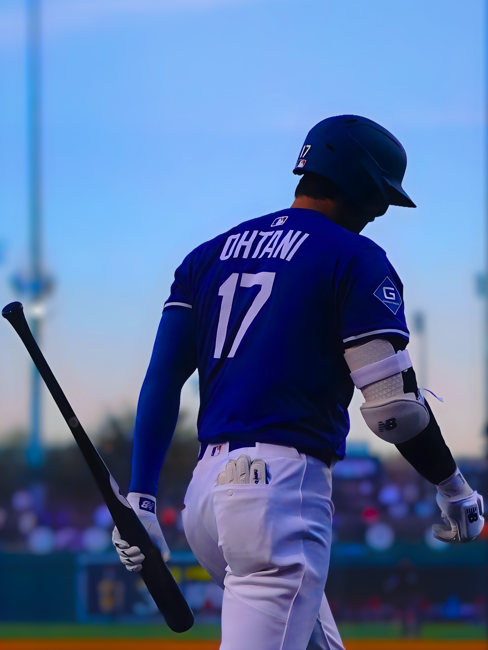 Shohei Ohtani in blue jersey with "OHTANI 17" on back, holding bat, walking on field.