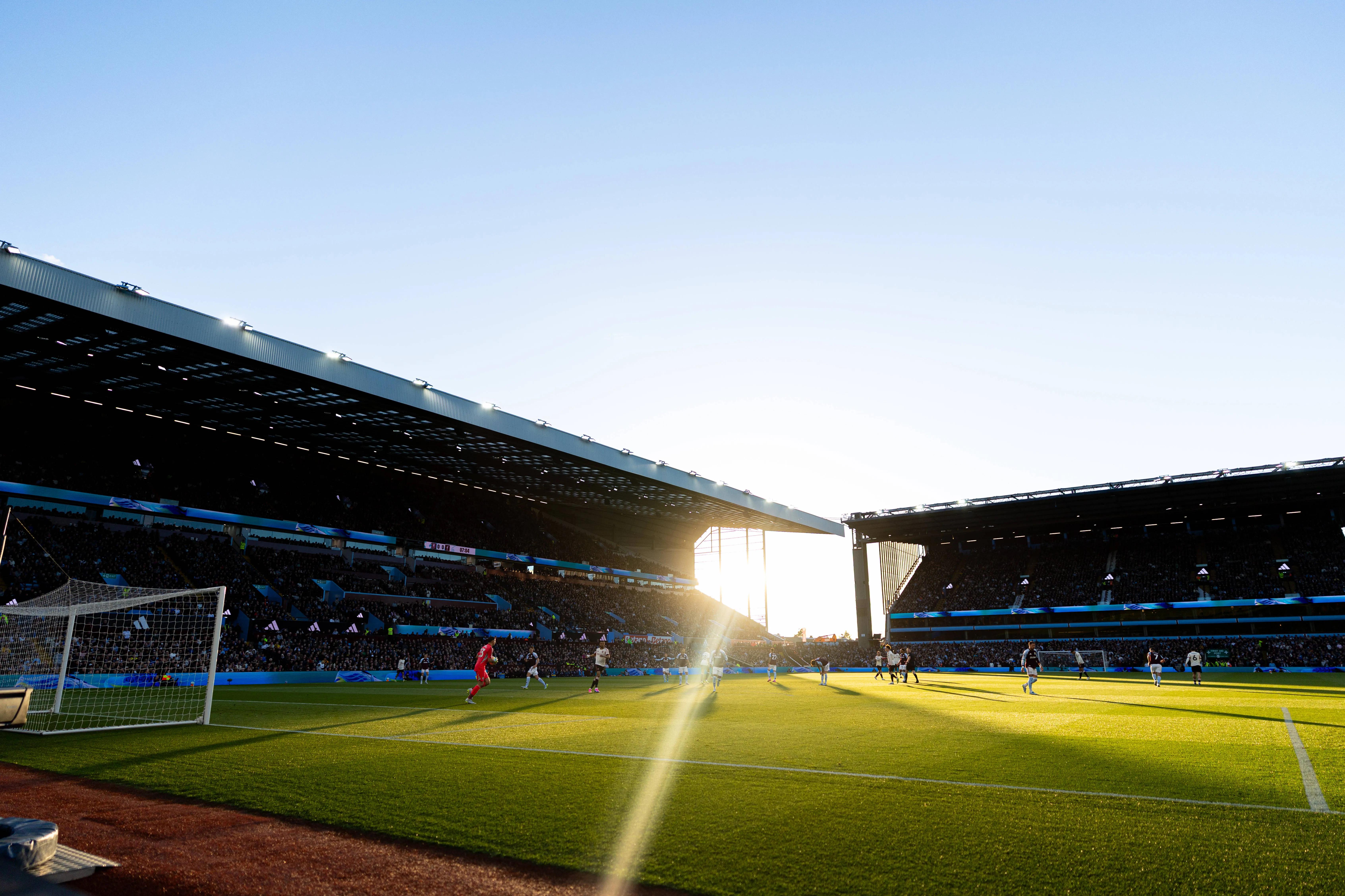Sunset flares over Villa Park hospitality stands as players compete on a golden hour soccer pitch.