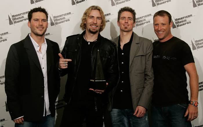 Nickelback smiling in front of an American Music Awards backdrop, Chad Kroeger holding an award