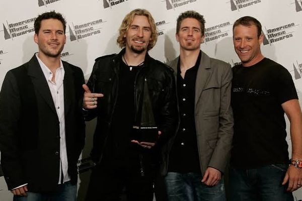 Nickelback smiling in front of an American Music Awards backdrop, Chad Kroeger holding an award