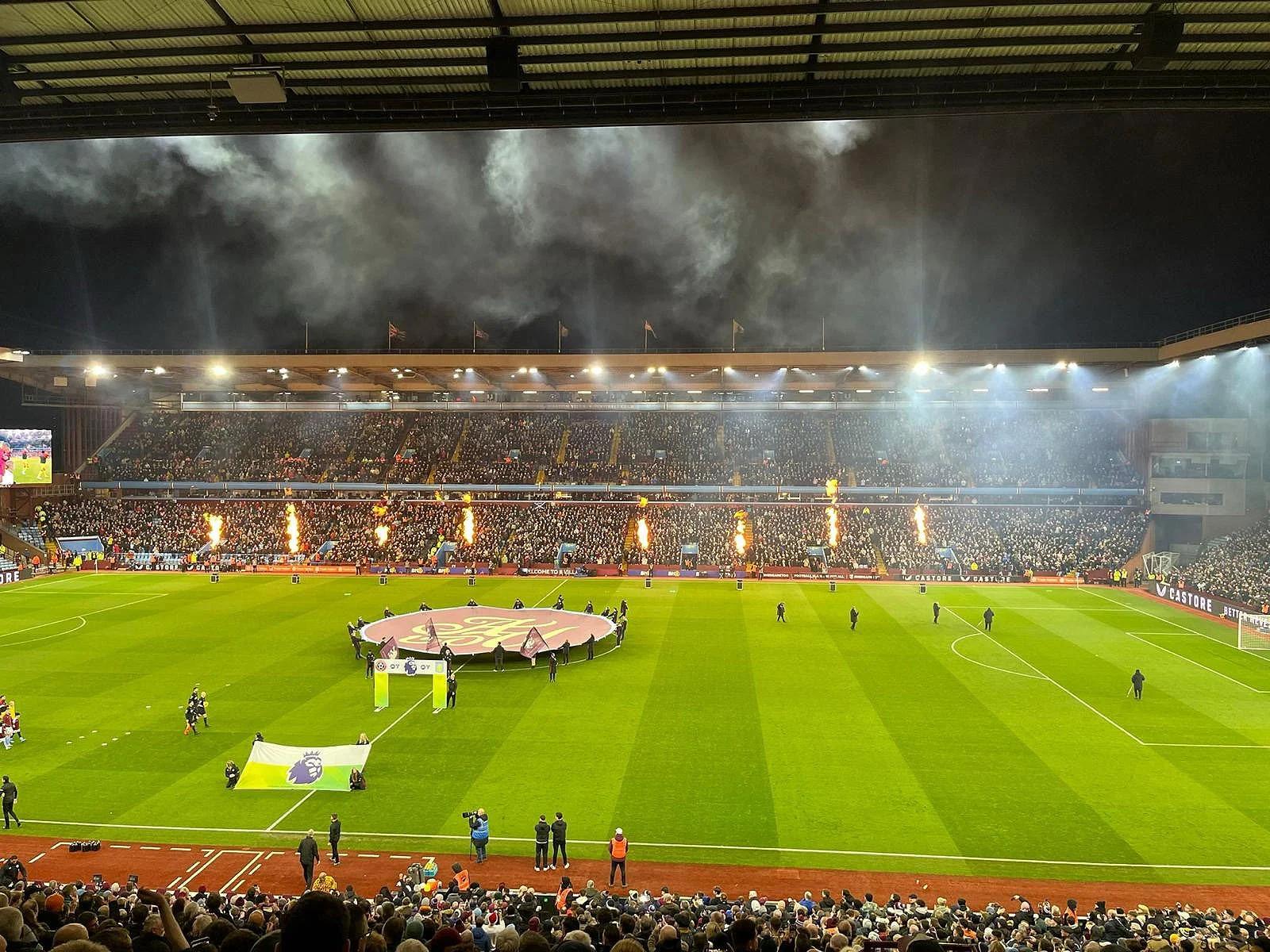 Aston Villa hospitality guests view flame cannons and banners during a night Premier League match.