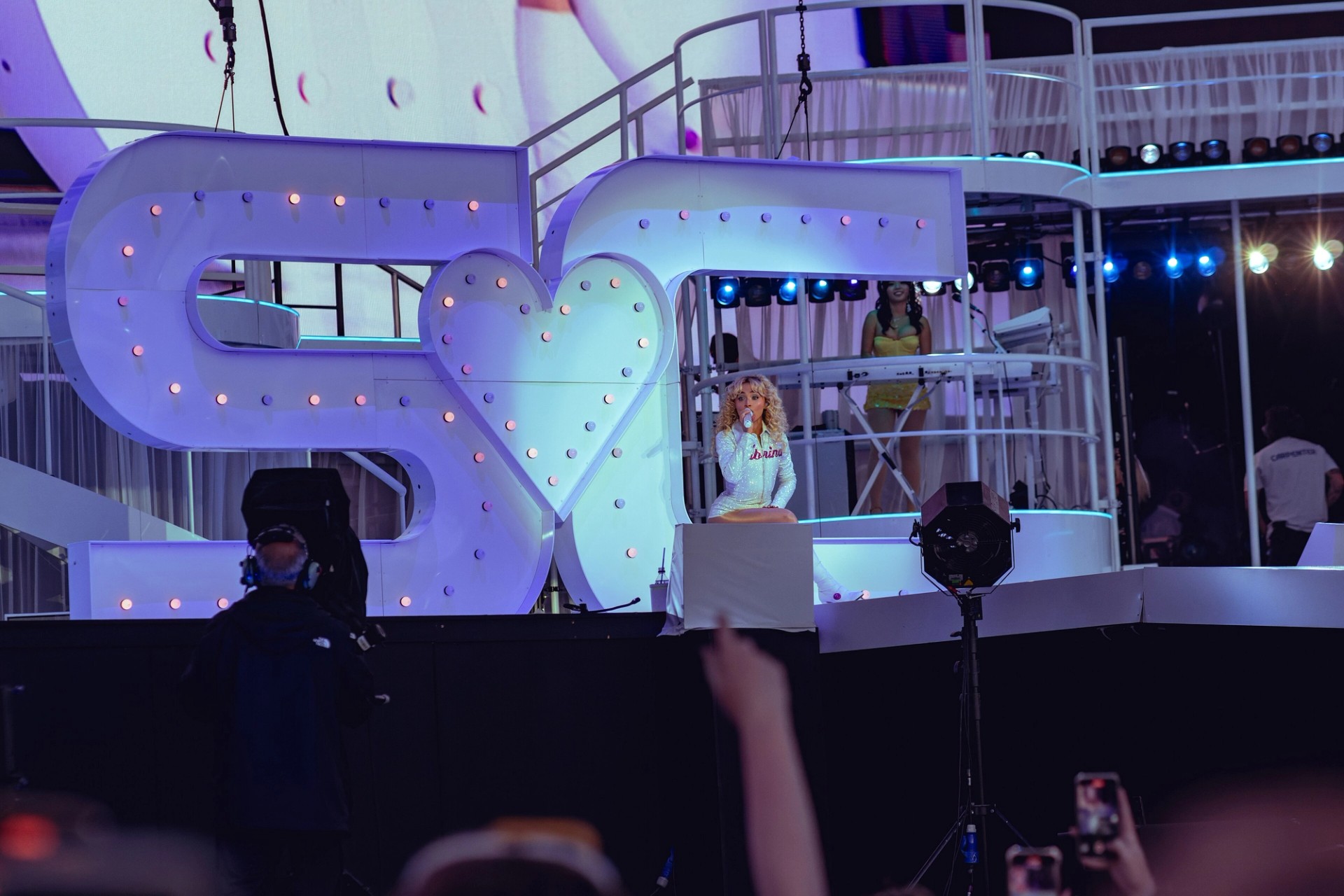 Sabrina Carpenter singing in a white sequinned outfit in front of a giant lit SC heart sign at BST Hyde Park in London, July 2025