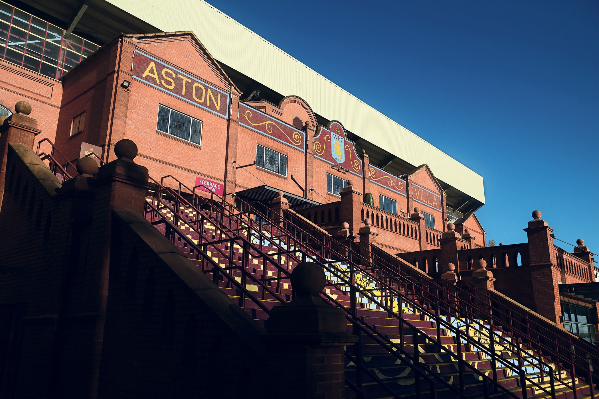 The Holte End at Villa Park features Aston Villa hospitality signs and the club's 1874 crest.