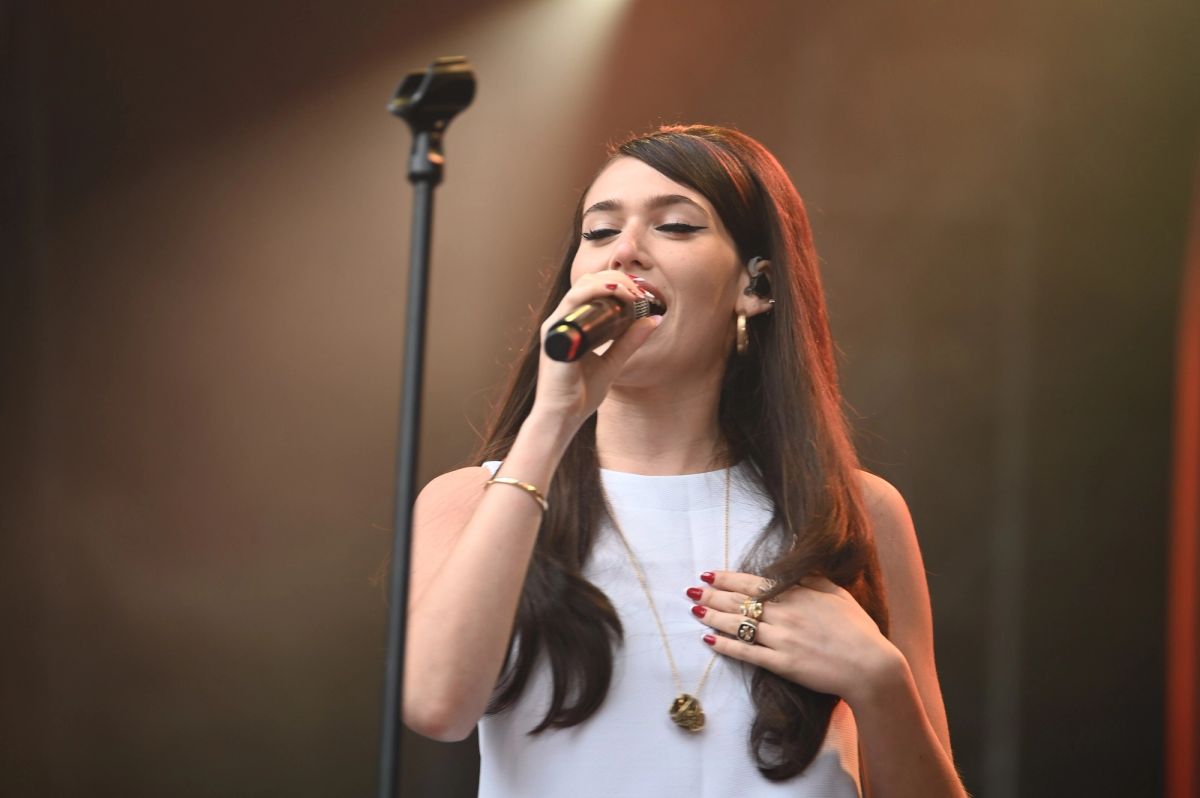 Sienna Spiro singing into a handheld microphone, wearing a white top