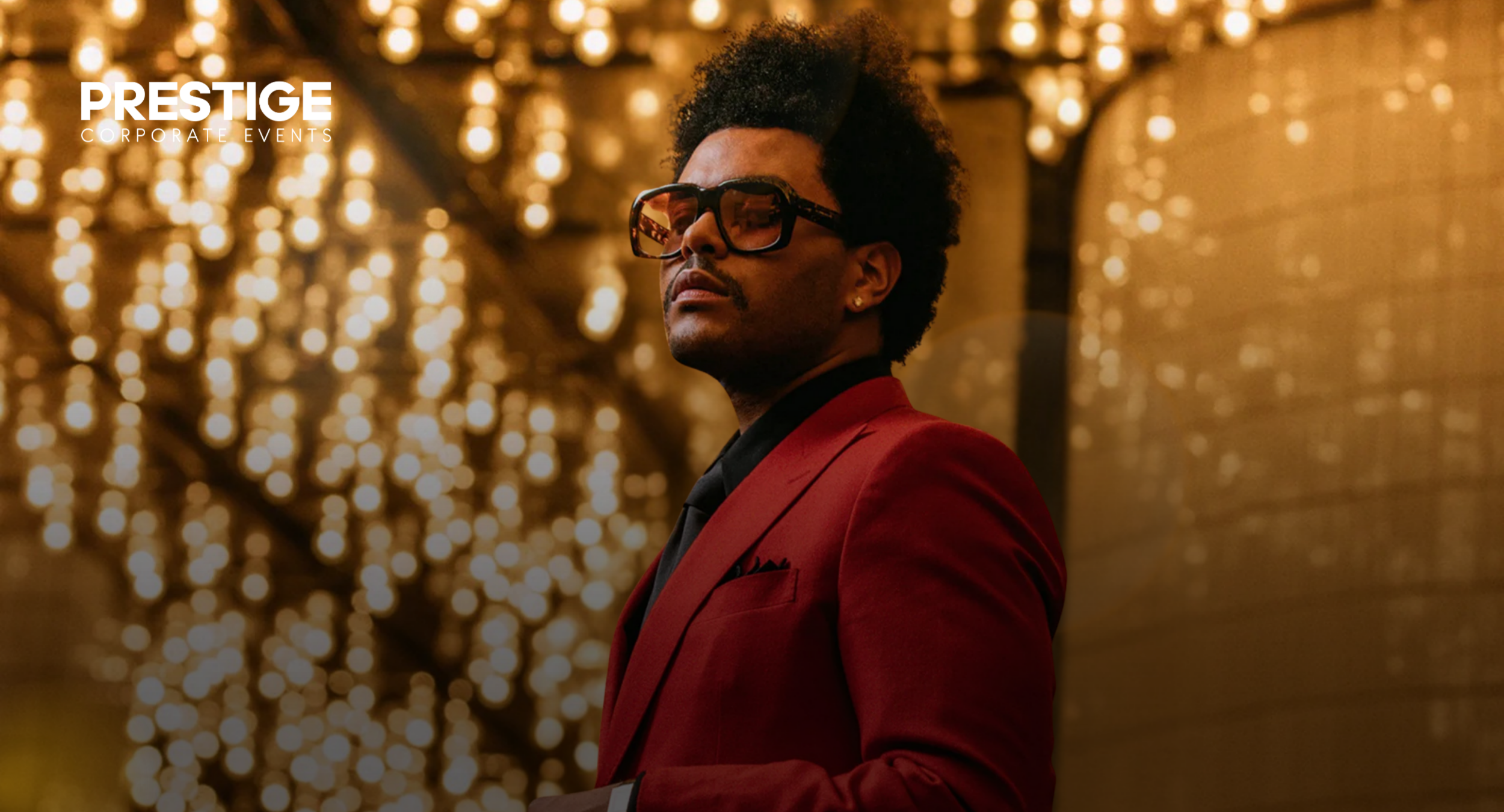 Abel Tesfaye at a prestige corporate event hospitality gala in a red suit with golden bokeh.
