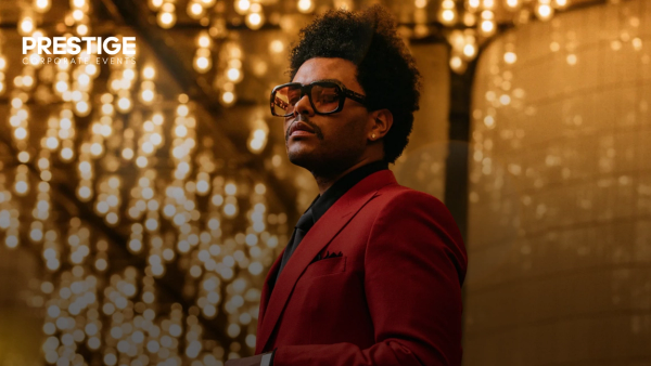Abel Tesfaye at a prestige corporate event hospitality gala in a red suit with golden bokeh.