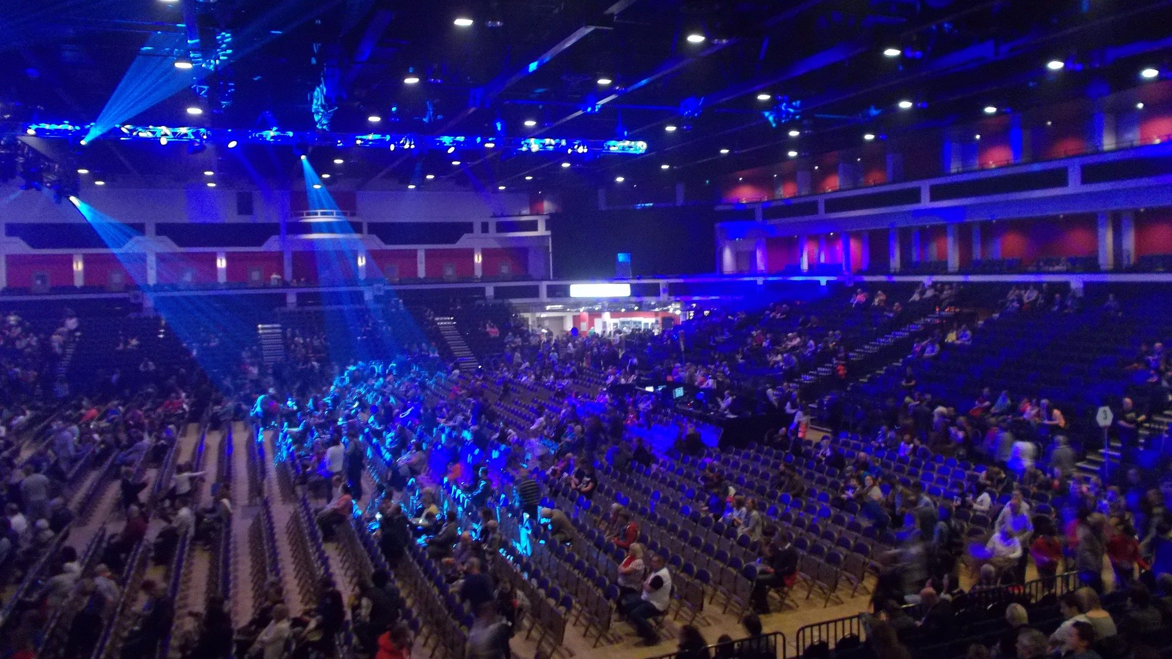 Audience finding their seats inside the arena in Cardiff before a concert, under blue stage lights