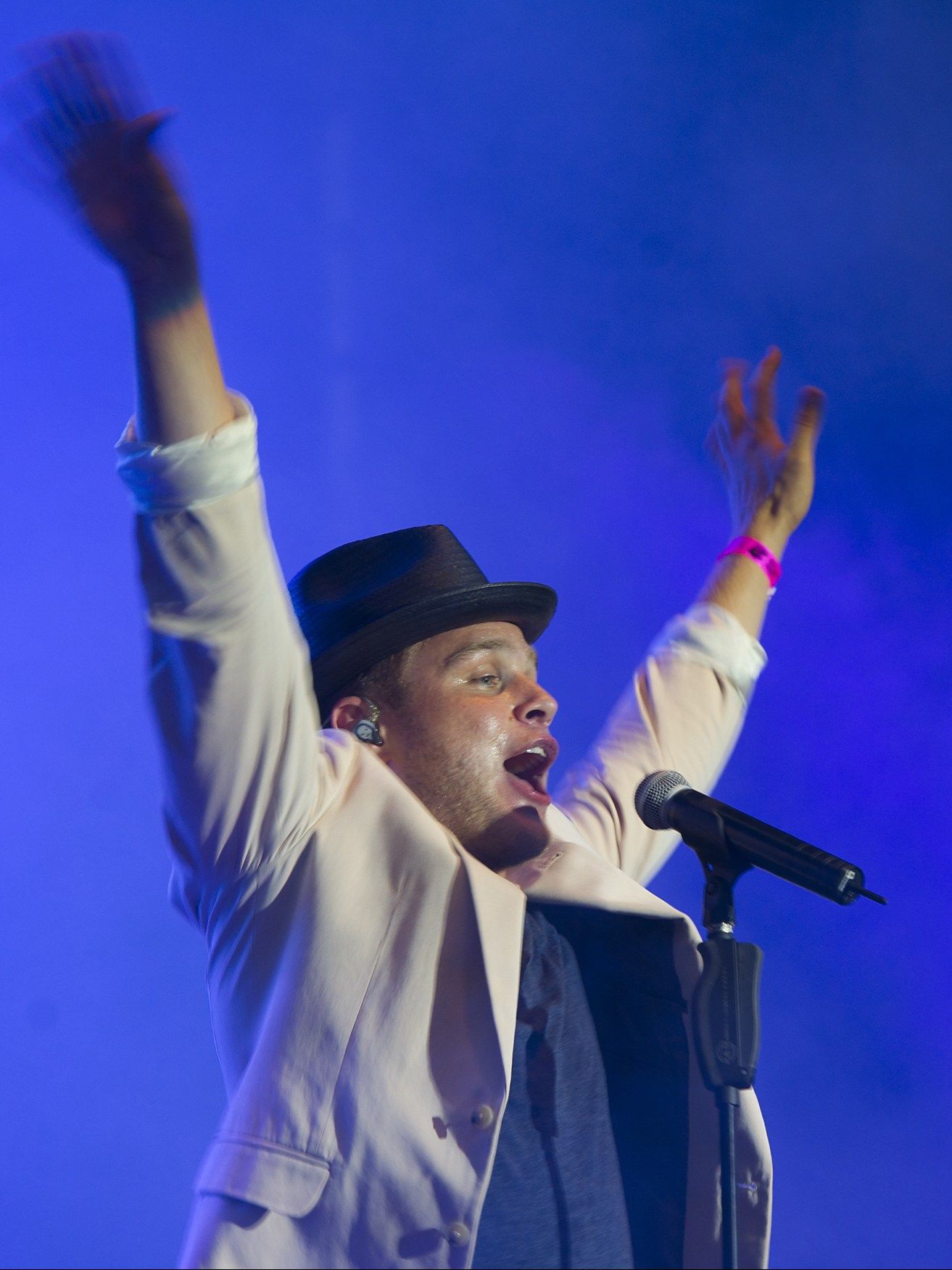Olly Murs with both arms raised, singing into a microphone stand under blue stage lights
